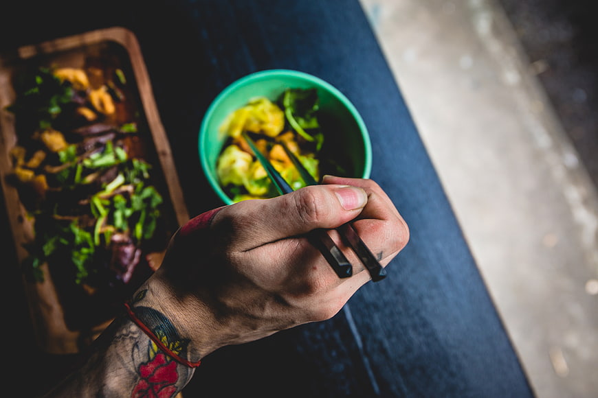 Tattooed Hand Holding Chopsticks Over Healthy Vegetable Bowl