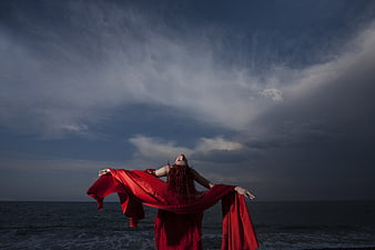 Woman in Red Cape Standing by Ocean Under Dramatic Sky
