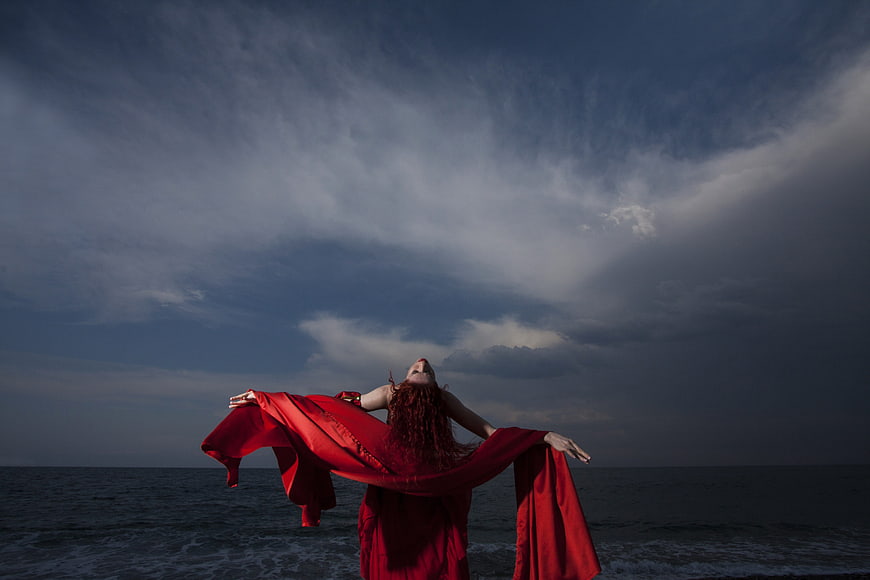 Woman in Red Cape Standing by Ocean Under Dramatic Sky