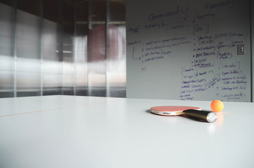 Table tennis paddle and ball on white table with whiteboard notes