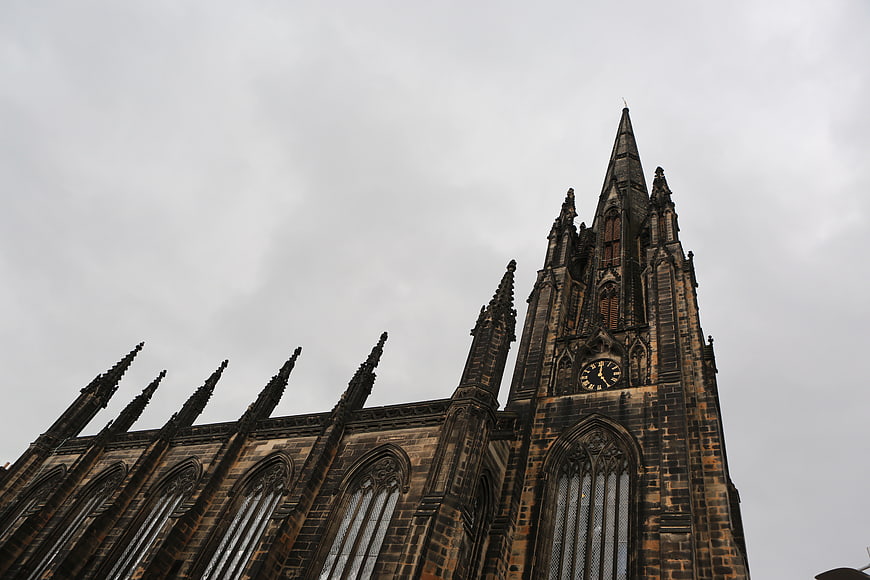 Gothic church spire and clock tower against cloudy sky