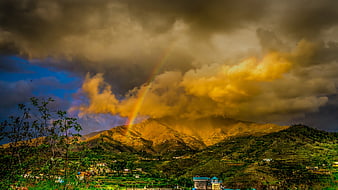 Dramatic Rainbow Over Mountainous Landscape with Golden Clouds