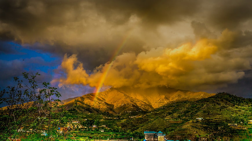Dramatic Rainbow Over Mountainous Landscape with Golden Clouds