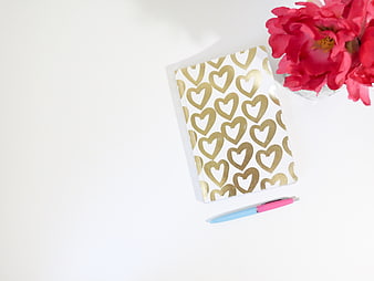 Flat lay of gold heart notebook with pink pen and red flowers