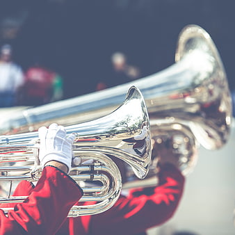 Close-up of brass band musicians playing silver tubas in red uniforms