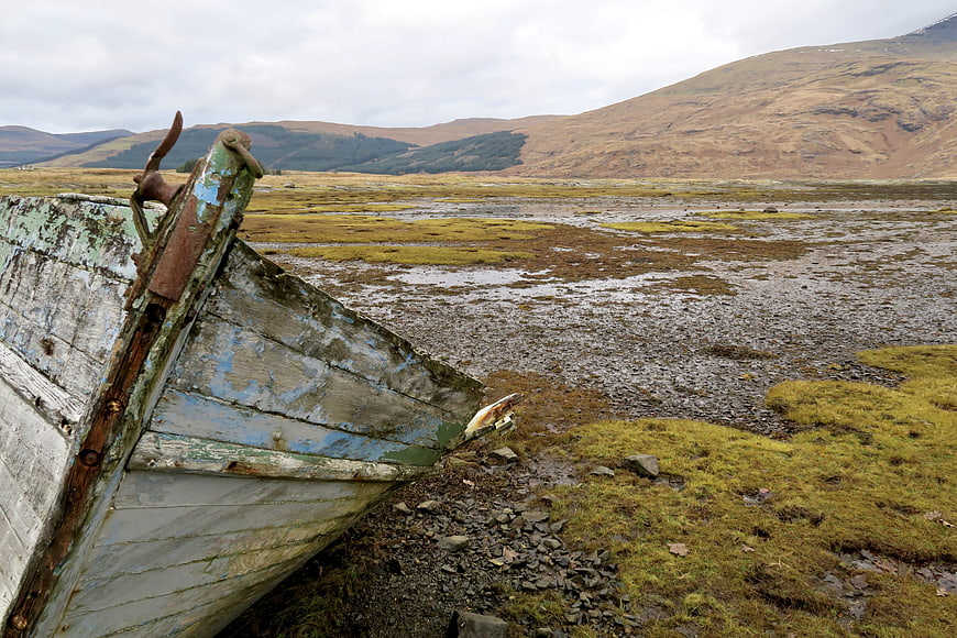 Weathered wooden boat on rocky shore with hills