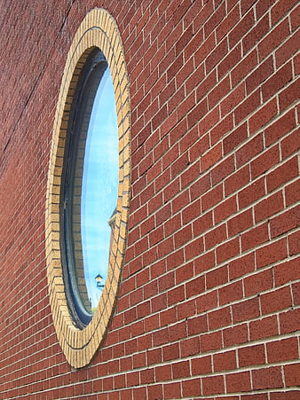 Red brick wall with oval window and blue sky reflection