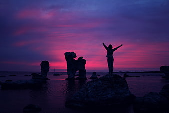 Silhouette of Woman with Arms Raised on Rocks at Sunset