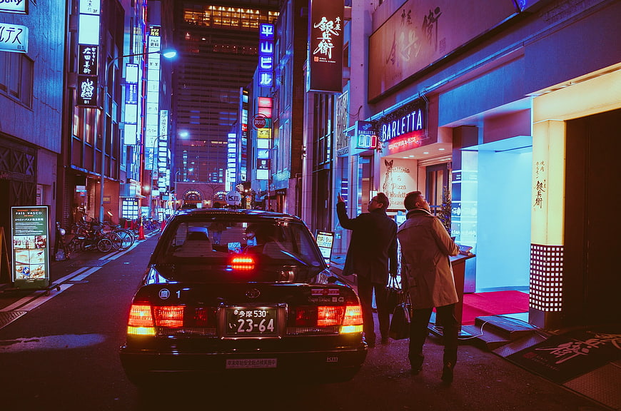 Black taxi and tourists in neon-lit Osaka street at night