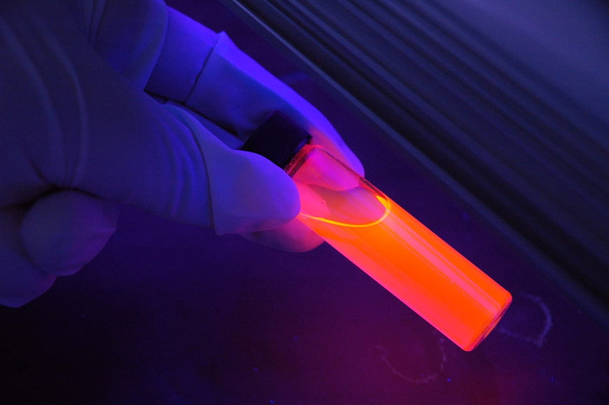 Gloved hand holding glowing orange test tube under UV light