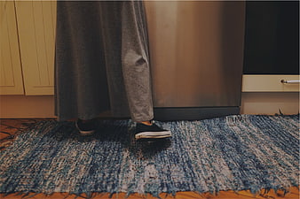 Person wearing sneakers standing on blue rug in kitchen