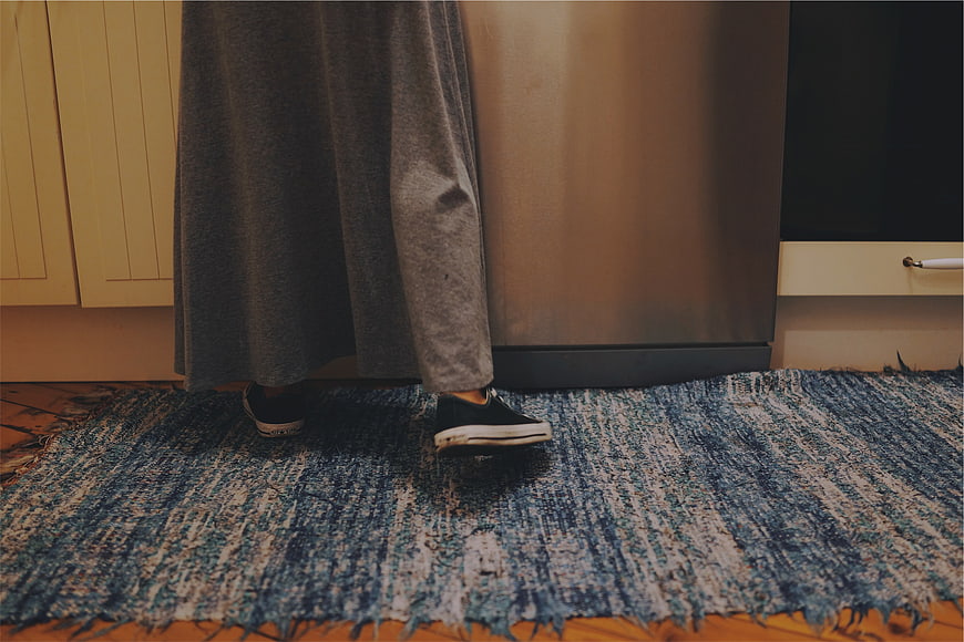 Person wearing sneakers standing on blue rug in kitchen