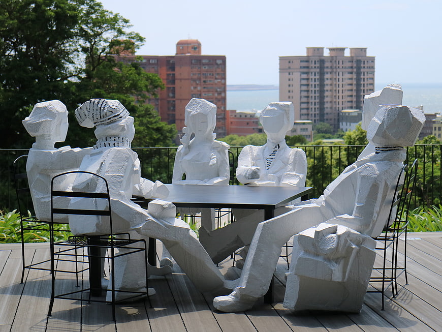 White Sculptural Figures Seated at Table on Rooftop Terrace