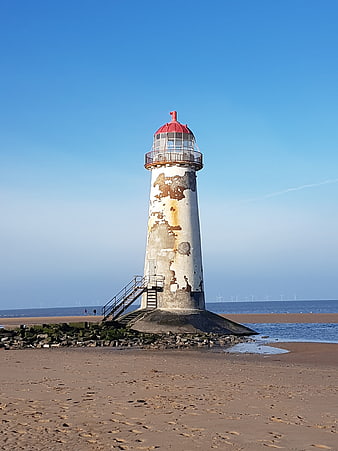 Weathered Lighthouse on Sandy Beach with Blue Sky