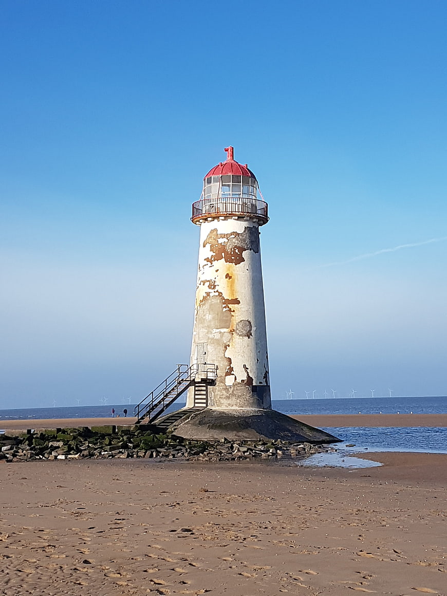 Weathered Lighthouse on Sandy Beach with Blue Sky