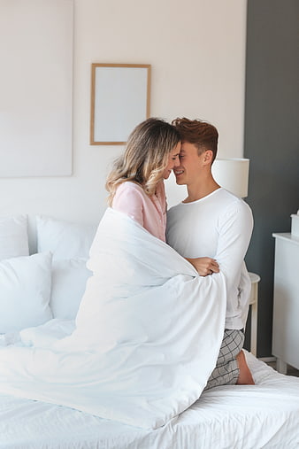 Happy couple cuddling in bed under white duvet