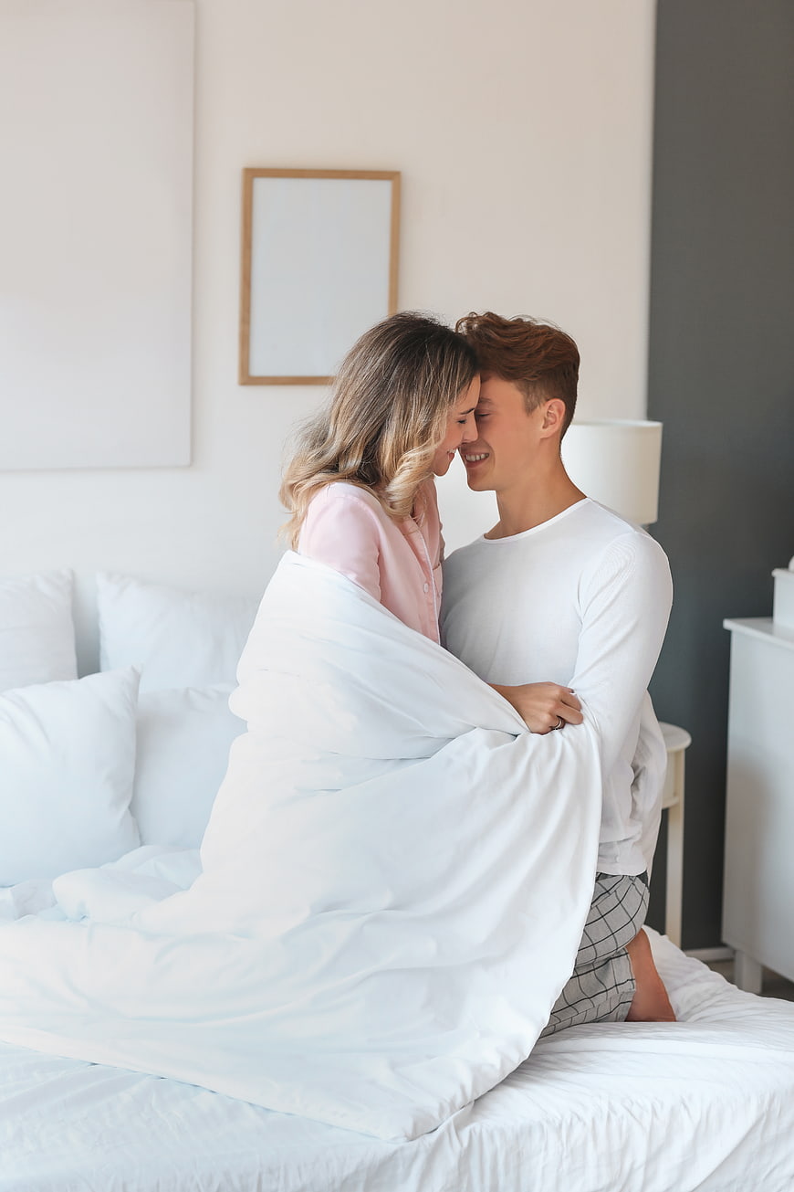 Happy couple cuddling in bed under white duvet