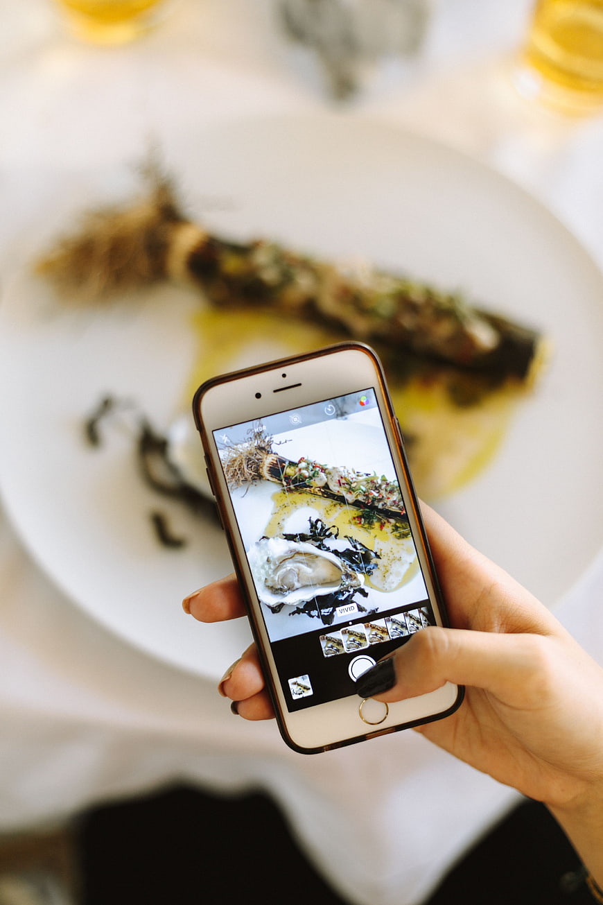 Hand holding smartphone photographing gourmet seafood dish