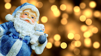 Blue Santa Claus Figurine Holding Teddy Bear Against Golden Bokeh Background