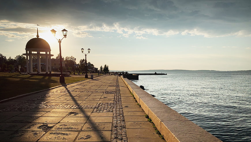Sunlit waterfront promenade with gazebo and calm lake