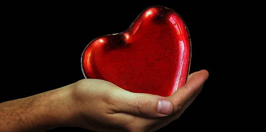 Hand Holding Shiny Red Heart on Black Background