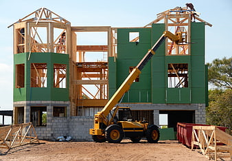 Construction site with yellow telehandler and unfinished house frame