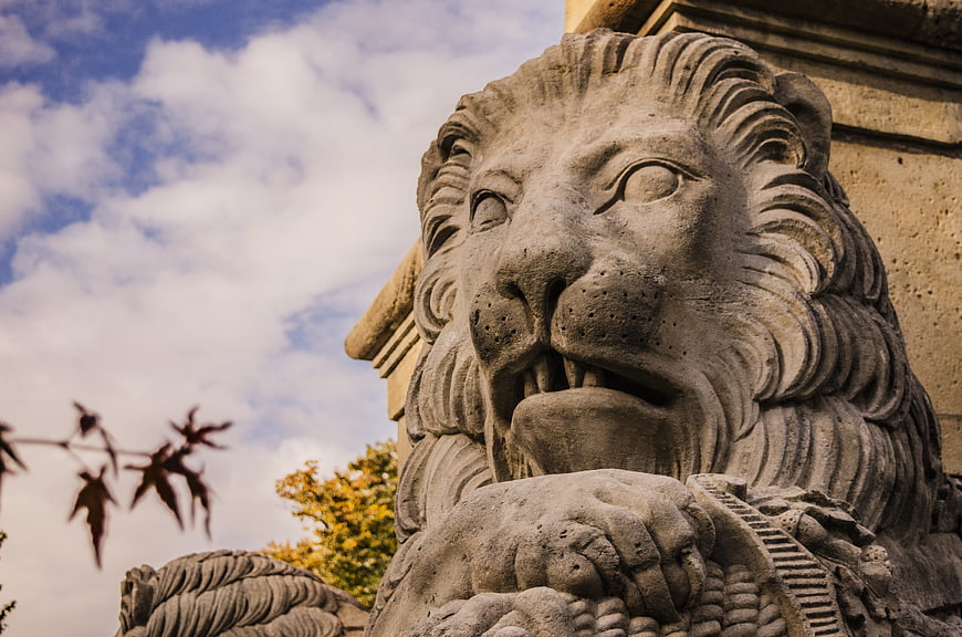 Close-up of weathered stone lion statue head against blue sky