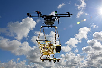 Drone Carrying Golden Shopping Cart Against Blue Sky
