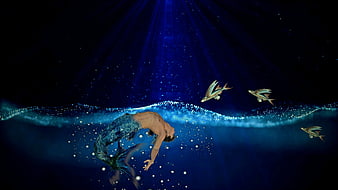 Mystical male merman swimming underwater with flying fish and light rays