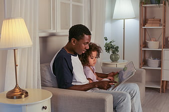 Father reading book to daughter on sofa at home