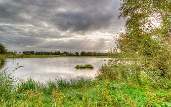 Dramatic cloudy sky over a calm lake with green meadows