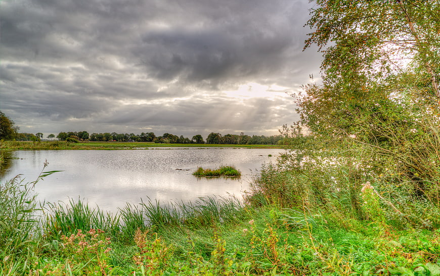 Dramatic cloudy sky over a calm lake with green meadows
