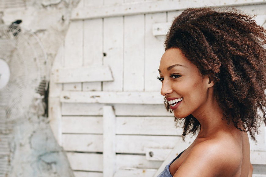 Smiling woman with curly hair against white wooden wall