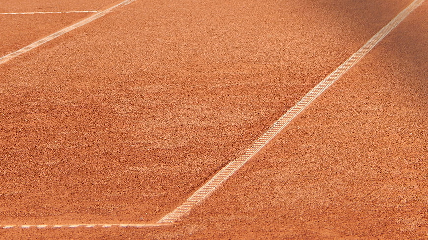 Close-up of red clay tennis court surface with white lines
