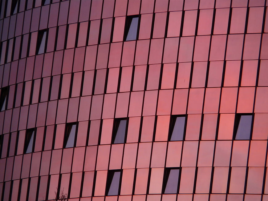 Modern glass building facade reflecting pink sunset sky