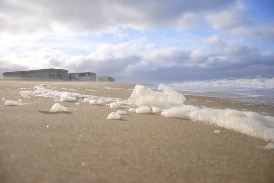 Low angle view of sea foam on sandy beach with ocean waves
