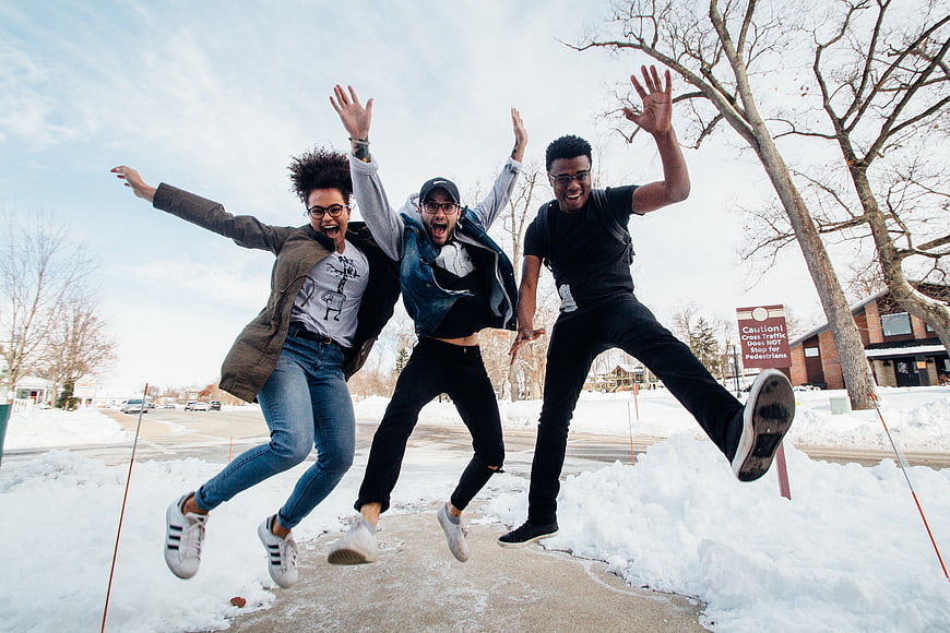 Diverse group of friends jumping in snow outdoors