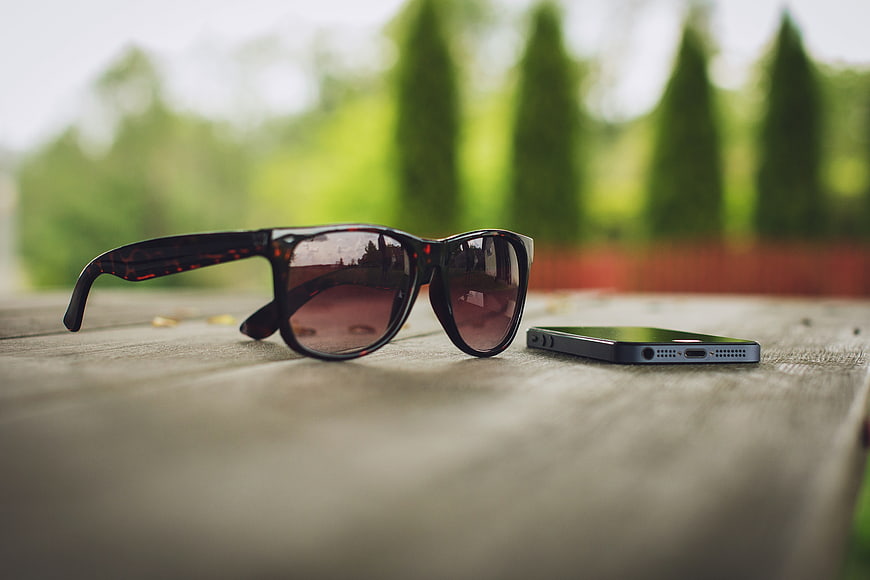 Sunglasses and Smartphone on Wooden Table Outdoors