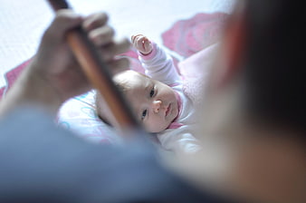 Baby looking up at parent holding wooden stick