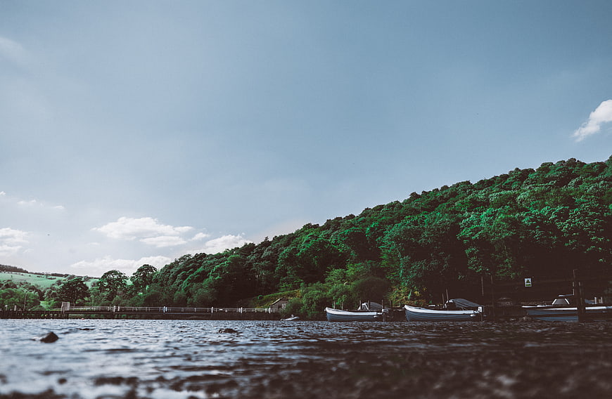 Boats Docked at Riverbank with Lush Green Hillside