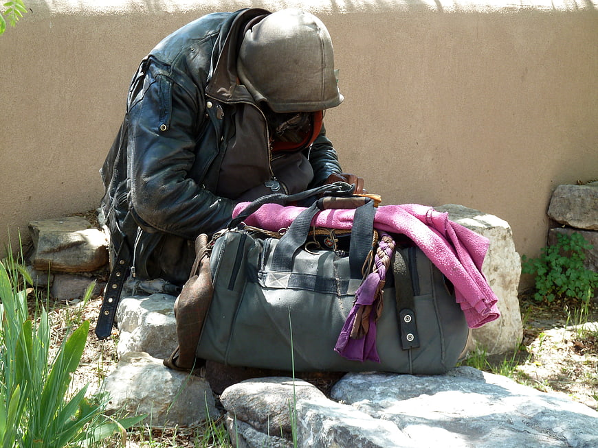 Homeless man sitting on rocks with a duffel bag outdoors