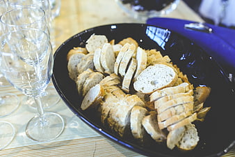 Sliced baguette bread in black bowl with wine glasses