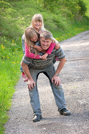 Grandfather giving piggyback rides to two girls on a country road