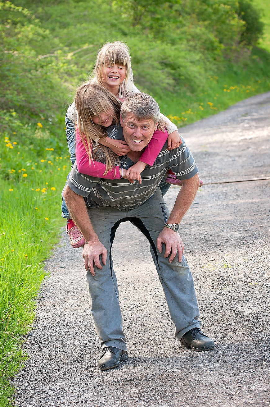 Grandfather giving piggyback rides to two girls on a country road