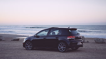Black Hatchback Car Parked on Sandy Beach at Sunset