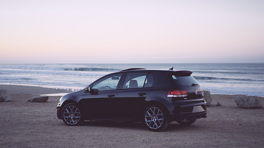 Black Hatchback Car Parked on Sandy Beach at Sunset