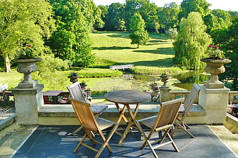 Wooden terrace furniture overlooking lush green park and pond