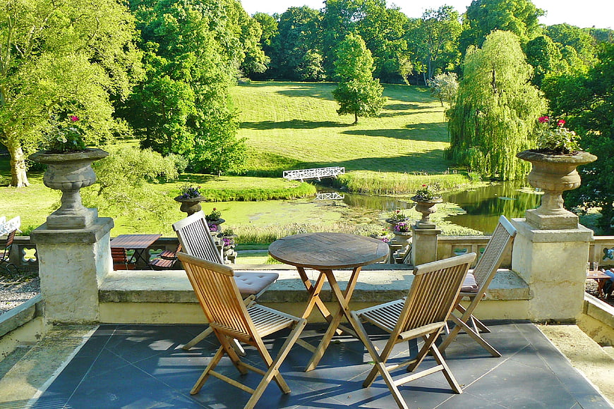 Wooden terrace furniture overlooking lush green park and pond