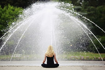 Woman meditating in front of a large water fountain spray