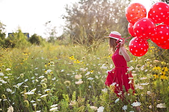 Young Woman in Red Dress Holding Balloons in Wildflower Meadow